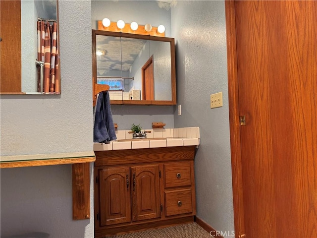 full bathroom featuring a textured wall, vanity, and baseboards