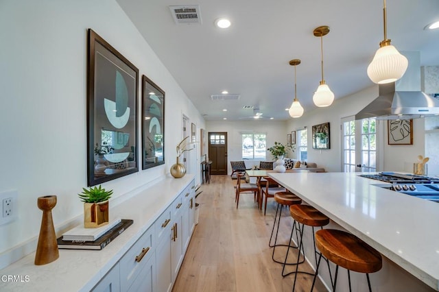 kitchen with a kitchen bar, decorative light fixtures, light stone countertops, light hardwood / wood-style floors, and white cabinets