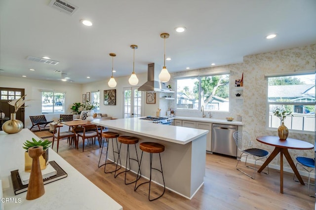 kitchen with sink, a breakfast bar area, hanging light fixtures, stainless steel appliances, and island exhaust hood