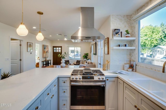 kitchen featuring sink, stainless steel gas stove, hanging light fixtures, white cabinetry, and island exhaust hood