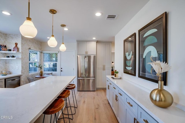 kitchen featuring pendant lighting, a kitchen breakfast bar, stainless steel appliances, light stone counters, and light hardwood / wood-style floors