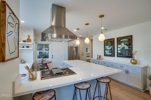 kitchen with a breakfast bar, island range hood, stainless steel fridge, hanging light fixtures, and light wood-type flooring