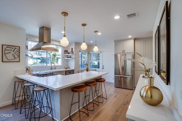 kitchen featuring a breakfast bar, hanging light fixtures, stainless steel appliances, island exhaust hood, and light wood-type flooring