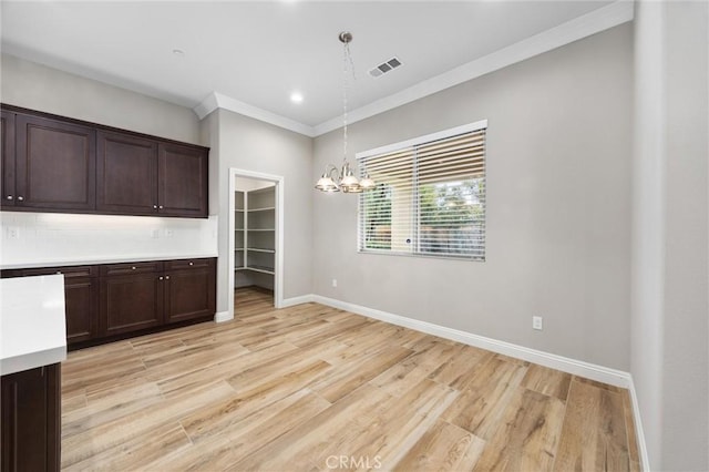 unfurnished dining area featuring dark brown cabinetry, decorative light fixtures, light hardwood / wood-style floors, and a chandelier