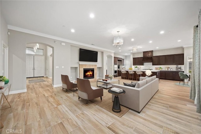 living room with a notable chandelier, ornamental molding, a fireplace, and light hardwood / wood-style floors