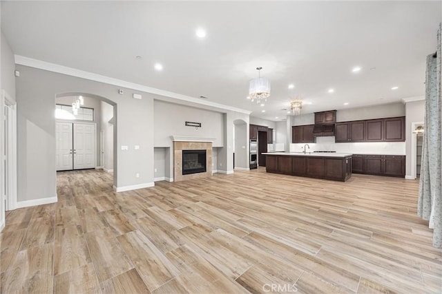 kitchen with decorative light fixtures, sink, a kitchen island with sink, light hardwood / wood-style floors, and crown molding