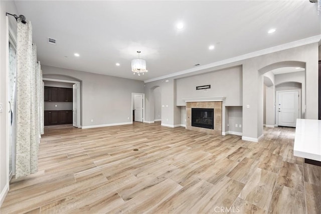 unfurnished living room featuring crown molding, a notable chandelier, a fireplace, and light wood-type flooring