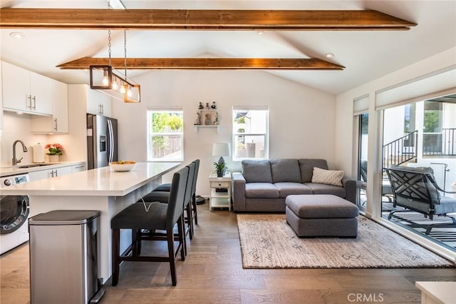 kitchen with sink, stainless steel fridge, a breakfast bar, white cabinetry, and hanging light fixtures