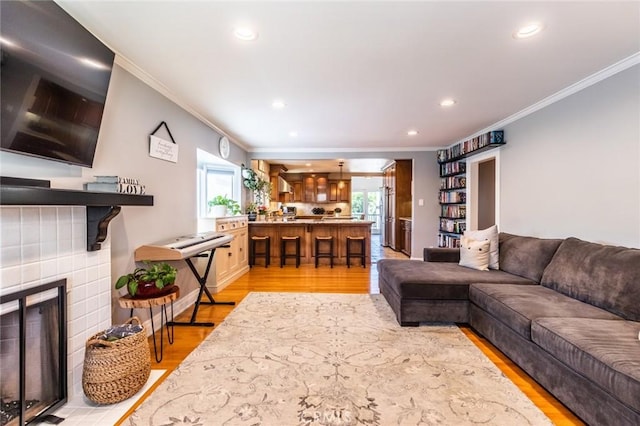 living room with crown molding, a tiled fireplace, and light wood-type flooring