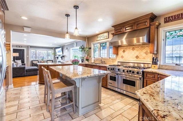 kitchen featuring range hood, a kitchen bar, range with two ovens, hanging light fixtures, and a center island