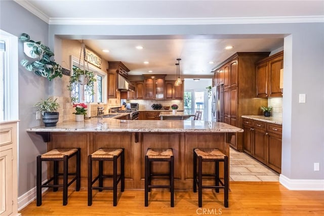 kitchen featuring stainless steel refrigerator, a breakfast bar area, stove, exhaust hood, and kitchen peninsula