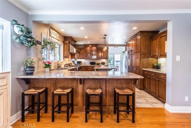 5333 Hartwick St, Los Angeles, CA 90041 - kitchen with under cabinet range hood, a peninsula, decorative backsplash, light stone counters, and appliances with stainless steel finishes