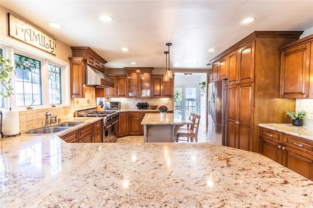 kitchen with sink, stainless steel appliances, light stone countertops, decorative backsplash, and decorative light fixtures