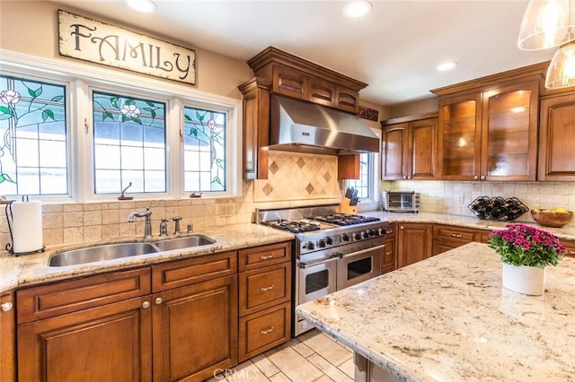 kitchen with sink, hanging light fixtures, extractor fan, decorative backsplash, and range with two ovens