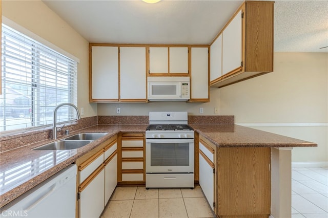 kitchen with sink, white appliances, white cabinets, light tile patterned flooring, and kitchen peninsula