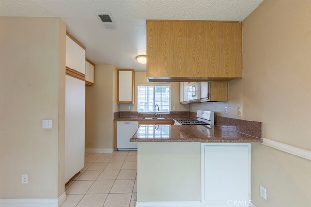 kitchen with sink, white appliances, light tile patterned floors, dark stone countertops, and kitchen peninsula