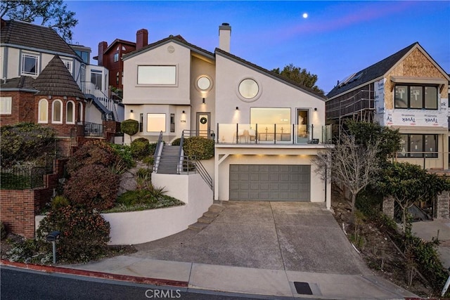 view of front of property featuring stucco siding, stairs, an attached garage, driveway, and a chimney