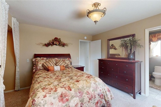 bedroom with light carpet, baseboards, and ensuite bath