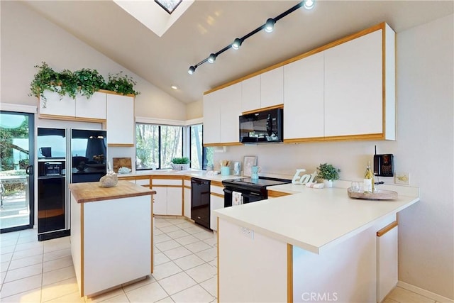 kitchen with white cabinets, a peninsula, vaulted ceiling with skylight, and black appliances