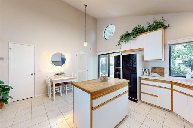 kitchen with white cabinetry, black fridge, light tile patterned floors, and hanging light fixtures