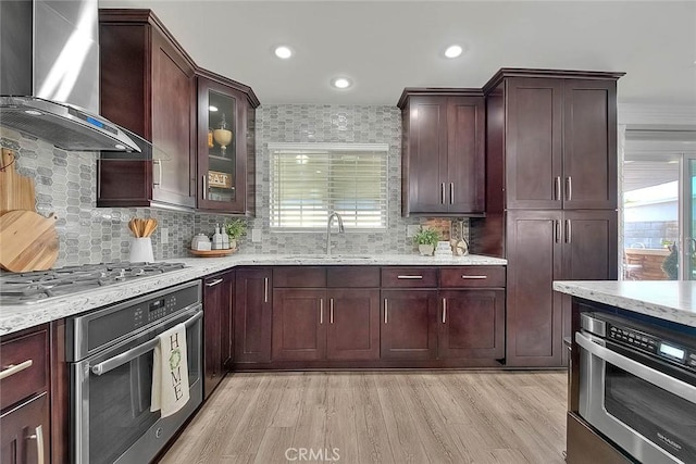 kitchen with sink, appliances with stainless steel finishes, plenty of natural light, wall chimney exhaust hood, and light wood-type flooring