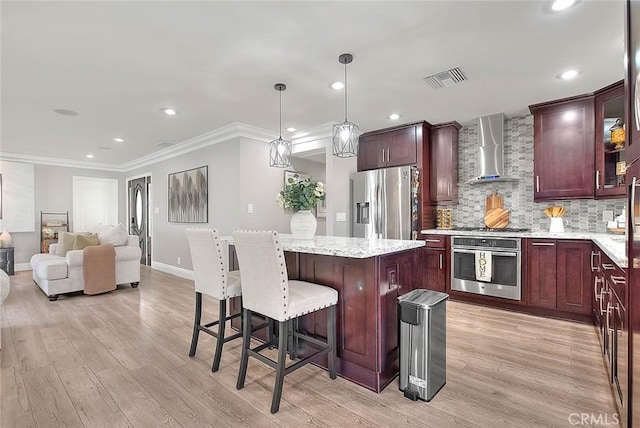 kitchen with a kitchen island, appliances with stainless steel finishes, pendant lighting, backsplash, and wall chimney exhaust hood