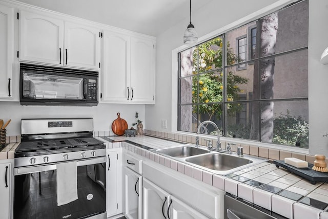 kitchen featuring tile countertops, sink, white cabinets, hanging light fixtures, and stainless steel gas range oven