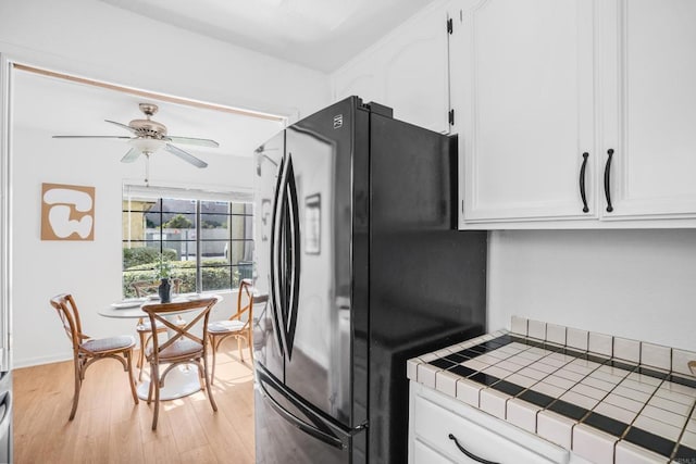 kitchen with light hardwood / wood-style flooring, ceiling fan, black refrigerator, white cabinetry, and tile countertops