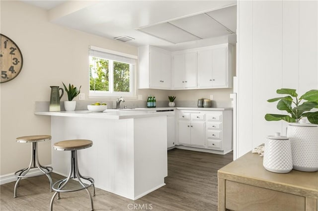 kitchen featuring dark hardwood / wood-style floors, a breakfast bar area, kitchen peninsula, and white cabinets