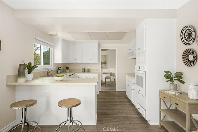 kitchen featuring a breakfast bar, sink, kitchen peninsula, white oven, and white cabinets