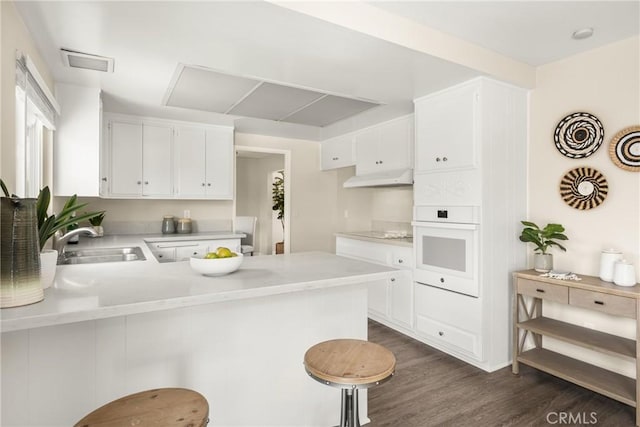 kitchen featuring dark hardwood / wood-style floors, white cabinetry, sink, kitchen peninsula, and white oven