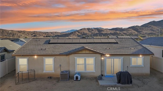 back house at dusk featuring solar panels, a mountain view, cooling unit, and a patio area