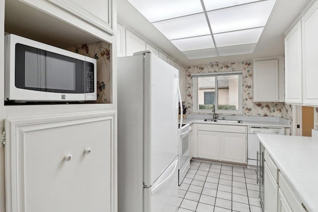 kitchen with white cabinetry, sink, light tile patterned floors, and white appliances