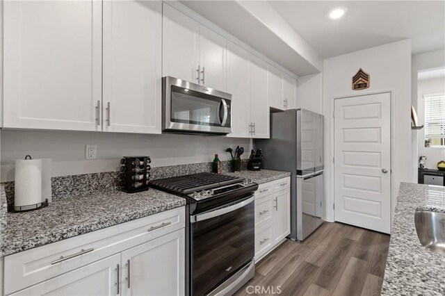 kitchen featuring light stone counters, dark wood finished floors, recessed lighting, appliances with stainless steel finishes, and white cabinetry