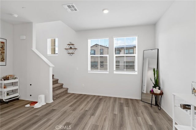 living room featuring light wood-style flooring, stairs, visible vents, and baseboards