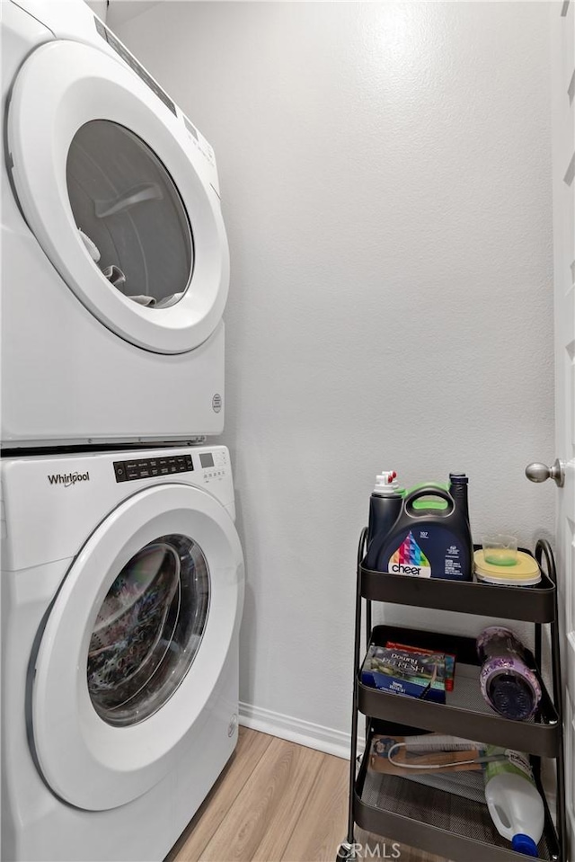 clothes washing area with stacked washer / dryer, laundry area, baseboards, and light wood finished floors