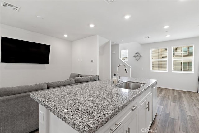 kitchen featuring a sink, white cabinets, open floor plan, light wood finished floors, and an island with sink