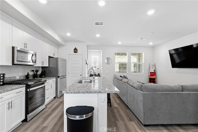 kitchen with stainless steel appliances, a sink, white cabinets, open floor plan, and an island with sink