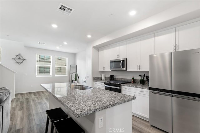 kitchen featuring light stone counters, stainless steel appliances, visible vents, a kitchen island with sink, and a sink