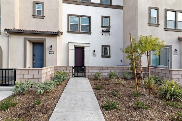 entrance to property with a gate, fence, and stucco siding