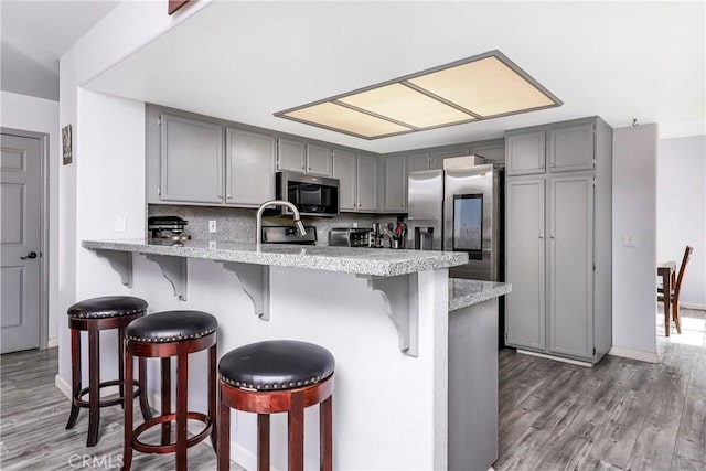 kitchen featuring a breakfast bar area, appliances with stainless steel finishes, gray cabinets, kitchen peninsula, and decorative backsplash