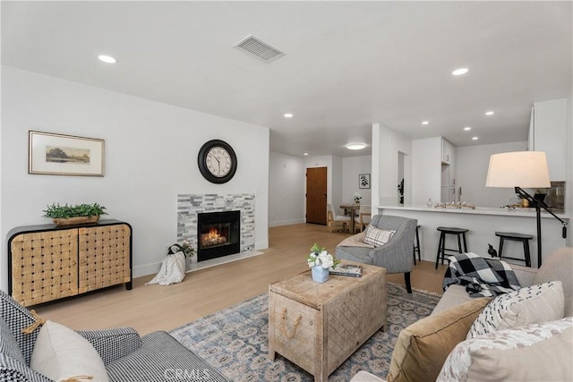 living room featuring light wood finished floors, baseboards, visible vents, a tile fireplace, and recessed lighting