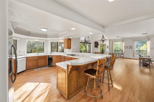 kitchen featuring tile countertops, brown cabinetry, light wood finished floors, and a peninsula