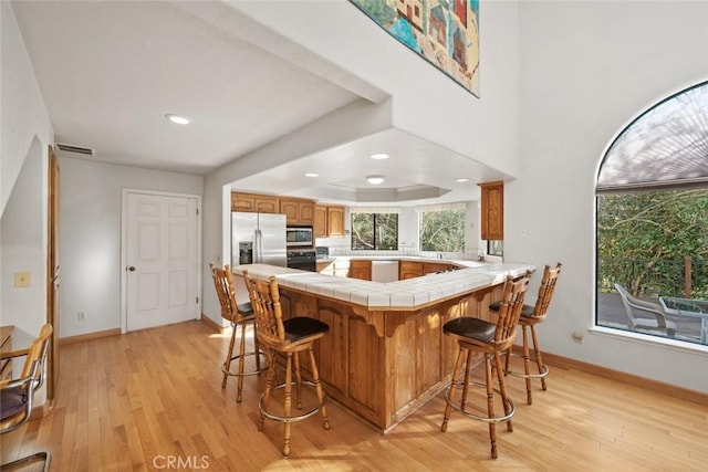 kitchen featuring tile counters, appliances with stainless steel finishes, light wood-style flooring, and a peninsula