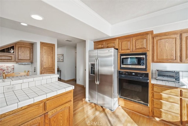 kitchen with a toaster, light wood finished floors, stainless steel appliances, and tile countertops