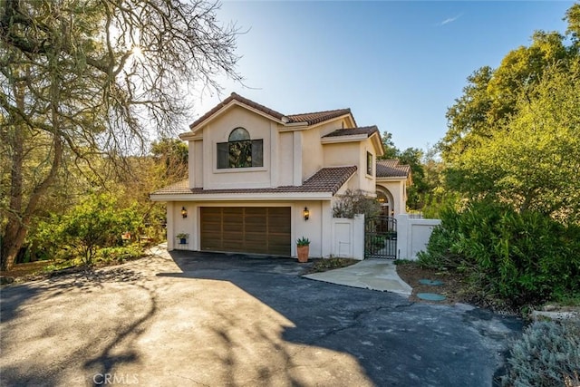view of front of home featuring a tiled roof, driveway, a gate, a garage, and stucco siding