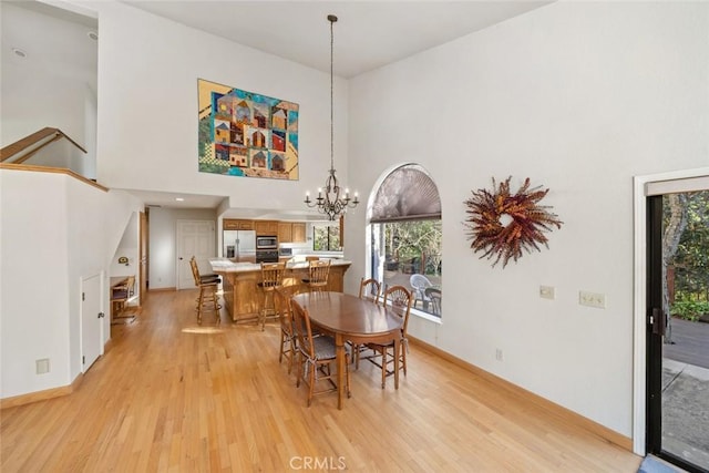 dining room with plenty of natural light, light wood-type flooring, a chandelier, and a towering ceiling