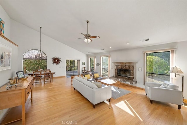 living area featuring visible vents, a fireplace, high vaulted ceiling, light wood-style flooring, and ceiling fan with notable chandelier