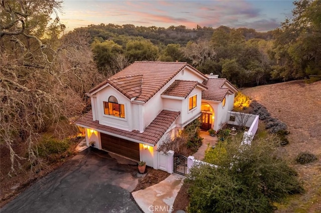 view of front of home featuring an attached garage, a tile roof, a view of trees, a gate, and fence private yard