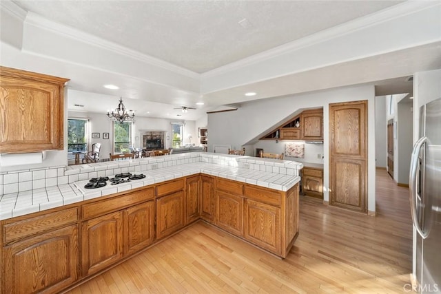 kitchen with brown cabinetry, light wood-type flooring, white gas cooktop, stainless steel fridge, and recessed lighting